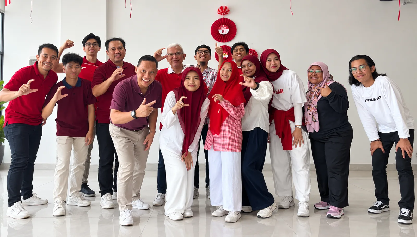 Sekitar lima belas orang berbaju merah dan putih tersenyum dan berpose bersama di kantor yang dihias untuk HUT RI